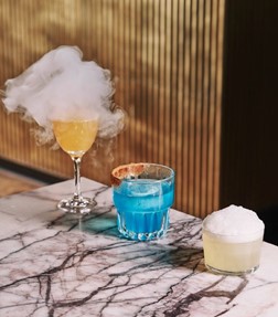 An image of three cocktails. One has smoke coming out of the top and one is blue