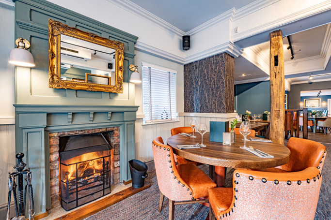 An image inside The Woodside. A round table in front of a log fire.