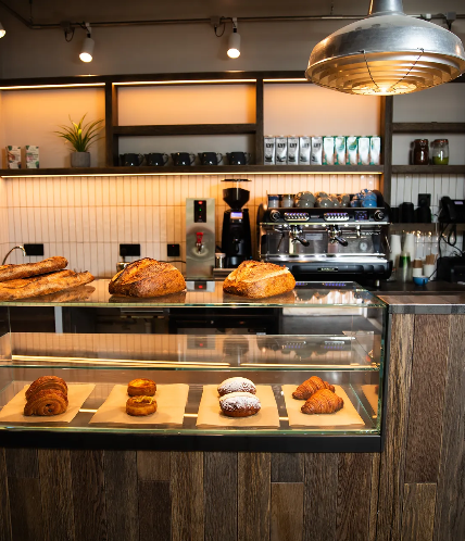 Photo of coffee counter with breads and pastries. Coffee machines and grinders in the background.