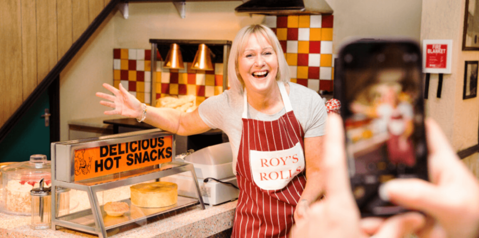 A woman wearing an apron having her photo taken on a mobile phone