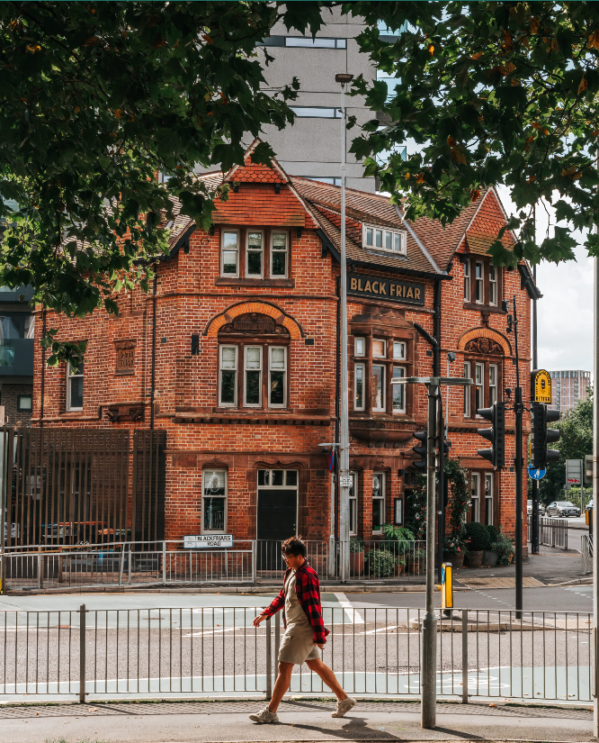 The Black Friar, a red brick pub and restaurant pictured with leafy trees in foreground, and a pedestrian walking